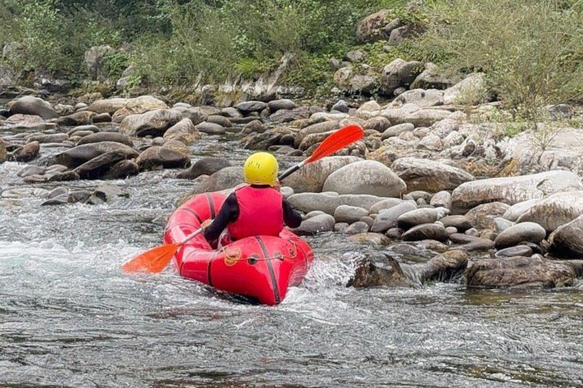 A person in a red raft navigating a river with rocks. 2