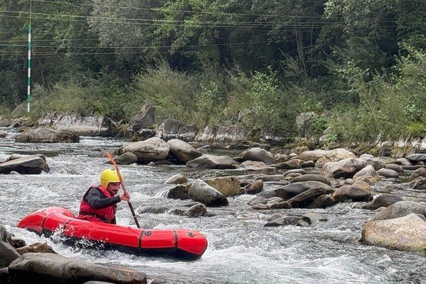 Una persona en un kayak rojo recorre un río con rocas grandes. 1