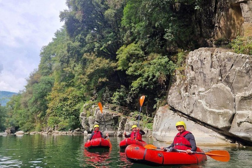 Three people kayaking on a calm river surrounded by rocky cliffs and dense greenery. 5
