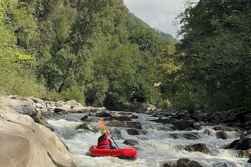 A person kayaking on a river surrounded by rocks and dense forest. 4
