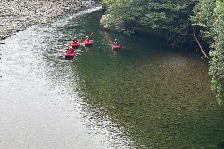 A group of people kayaking on a calm river surrounded by trees. 3