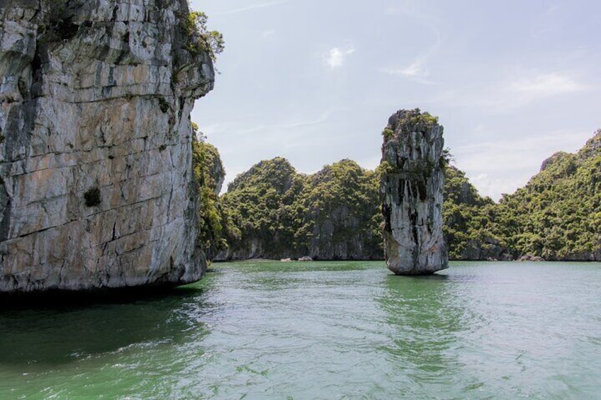 A large rock formation in a body of water with a forested island in the background. 2