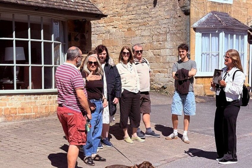 A group of people standing on a paved street in front of a stone building with a window and a door. 4