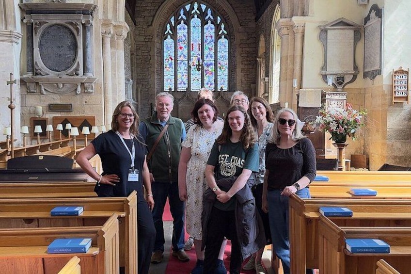 A group of people standing in a church with stained glass windows and wooden pews. 1