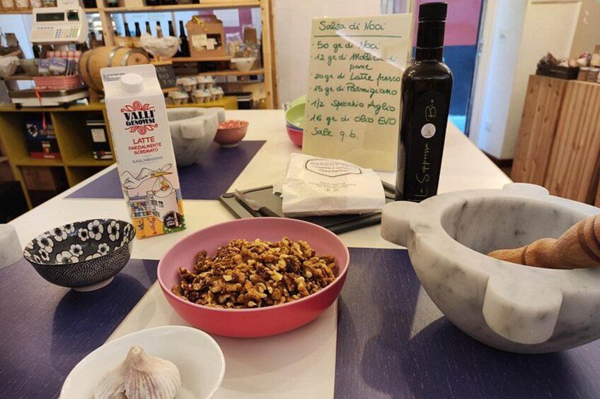 Una mesa con un cuenco de frutos secos, una botella de aceite de oliva, un cartón de leche y un cartel con una lista de ingredientes. 2