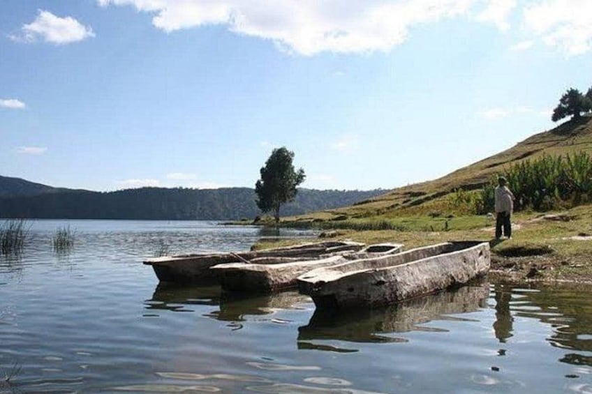 A calm lake with a person standing on the shore, a tree, and a boat. 1