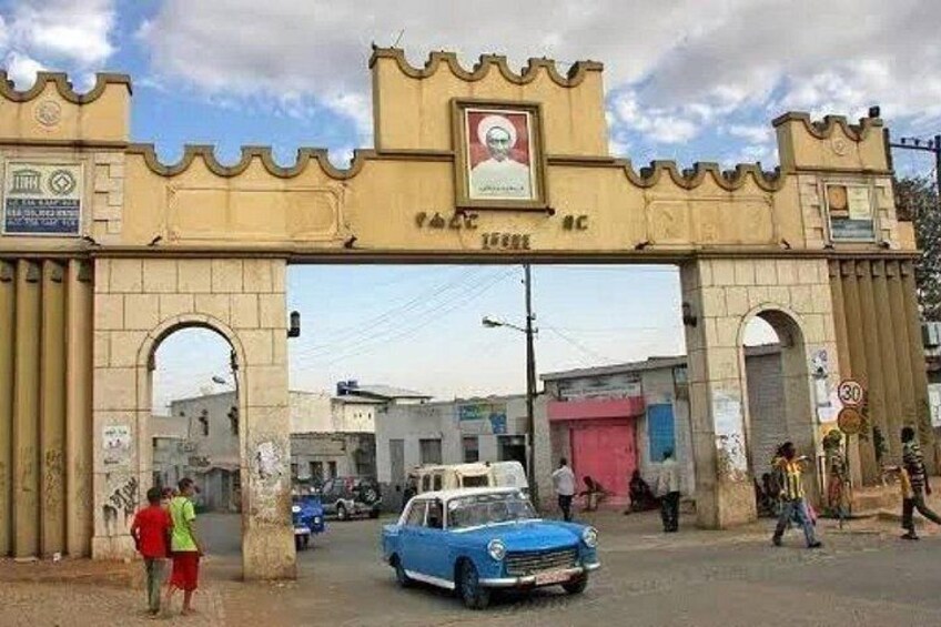 A street scene with a large archway, a blue car, and pedestrians. 2