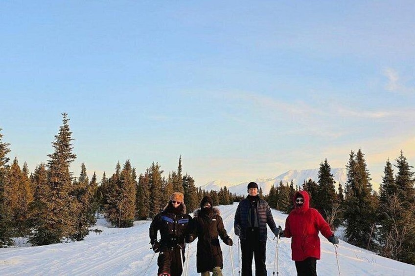 Un grupo de personas esquiando de fondo en un sendero nevado, con árboles y montañas al fondo. 4
