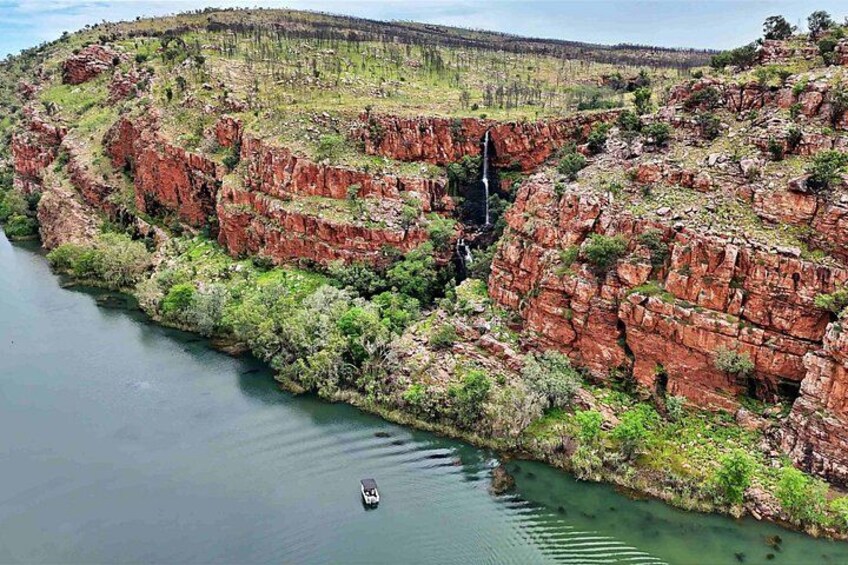Ein Fluss schlängelt sich durch eine Schlucht mit roten Felsformationen und einem Wasserfall. 2