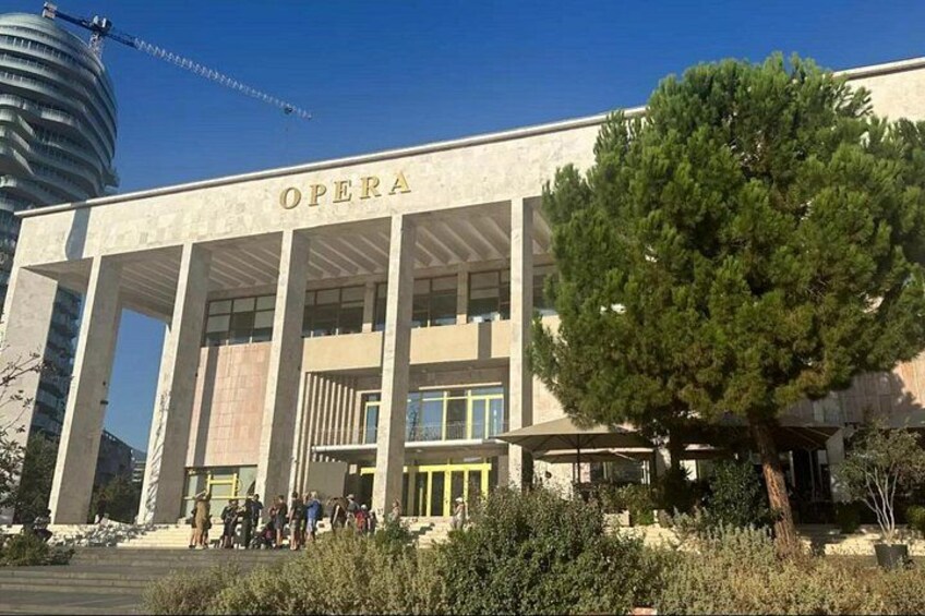 Ein Gebäude mit dem Schriftzug 'OPERA', umgeben von Bäumen und bewölktem Himmel. 4