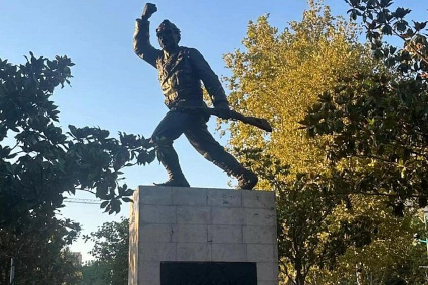 Eine Statue, die eine Person mit einem Baseballschläger auf einem Sockel darstellt, umgeben von Bäumen. 2