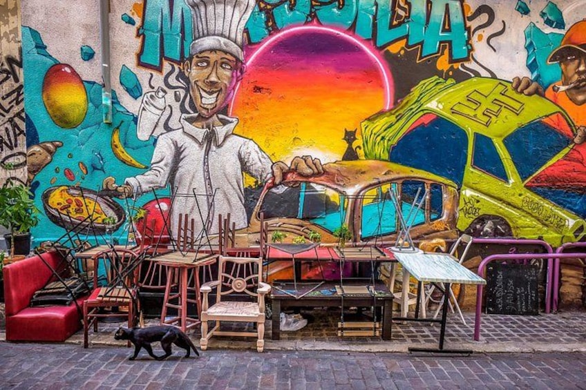 A street with a mural, chairs, tables, and a dog. 2