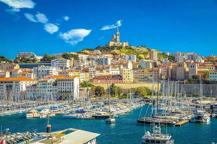 A coastal town with a marina filled with boats, historic buildings, and a prominent hilltop structure. 3