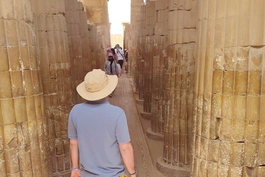 A person walking through a narrow passageway flanked by large stone columns. 1