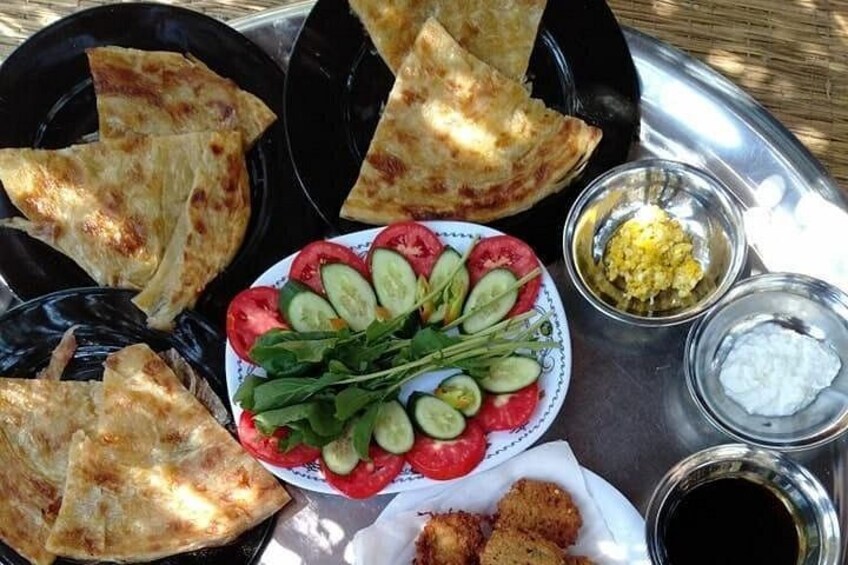 A meal with pita bread, sliced tomatoes, cucumbers, a salad, and two bowls of sauce. 5