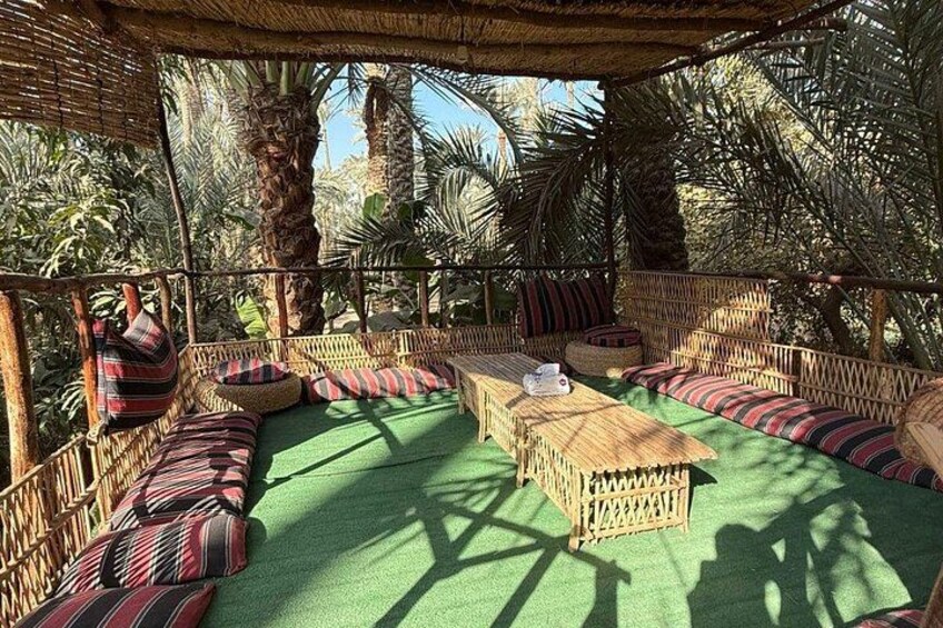 A covered outdoor seating area with woven furniture and cushions, surrounded by palm trees. 3