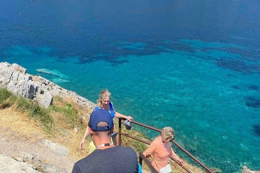 Paisaje costero con aguas azul cristalino, terreno rocoso y una persona bajando una escalera. 5