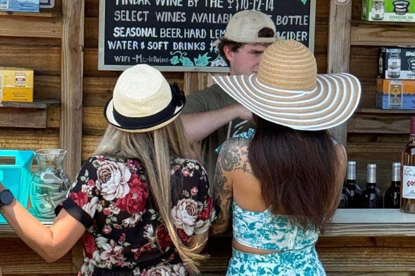 Dos personas en un bar, una sosteniendo una bebida. Hay estantes con botellas y un letrero con texto. 2