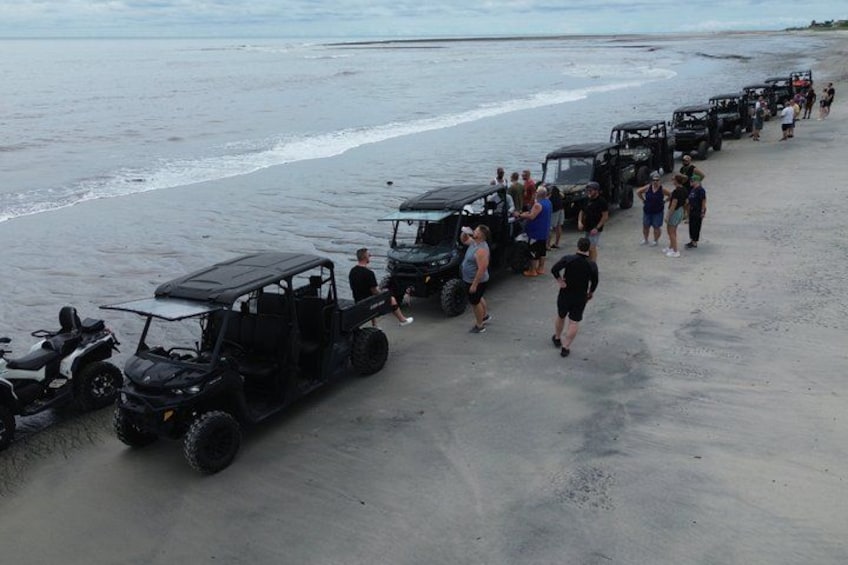 A beach with ATVs lined up and people walking. 1