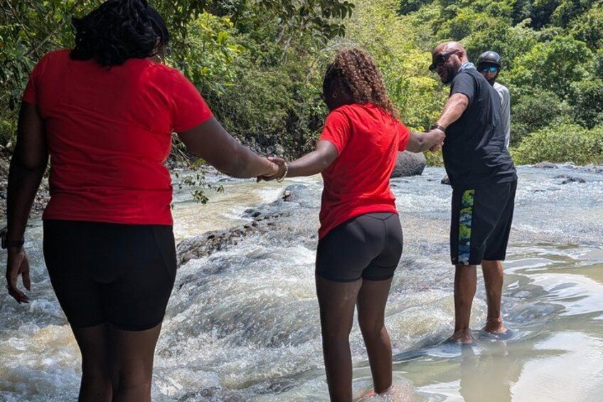 People holding hands near a flowing river in a forested area. 5