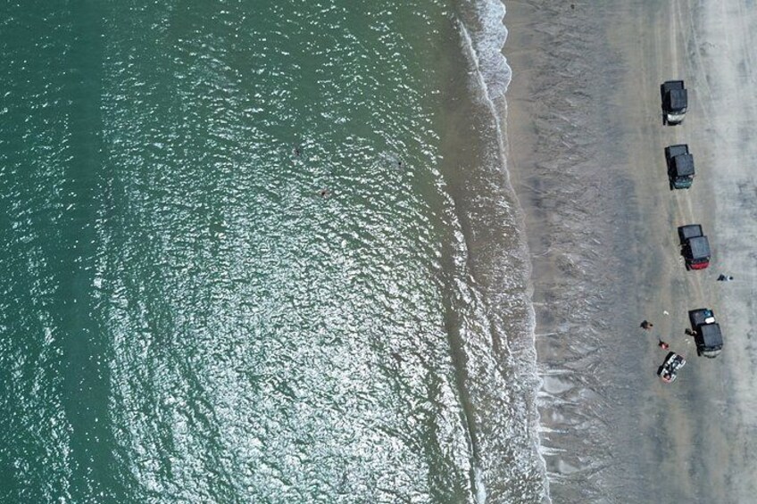 An aerial view of a beach with cars parked along the shore and waves approaching the beach. 4