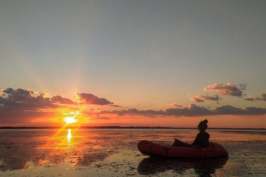 A sunset over a body of water with a person in a raft. 1