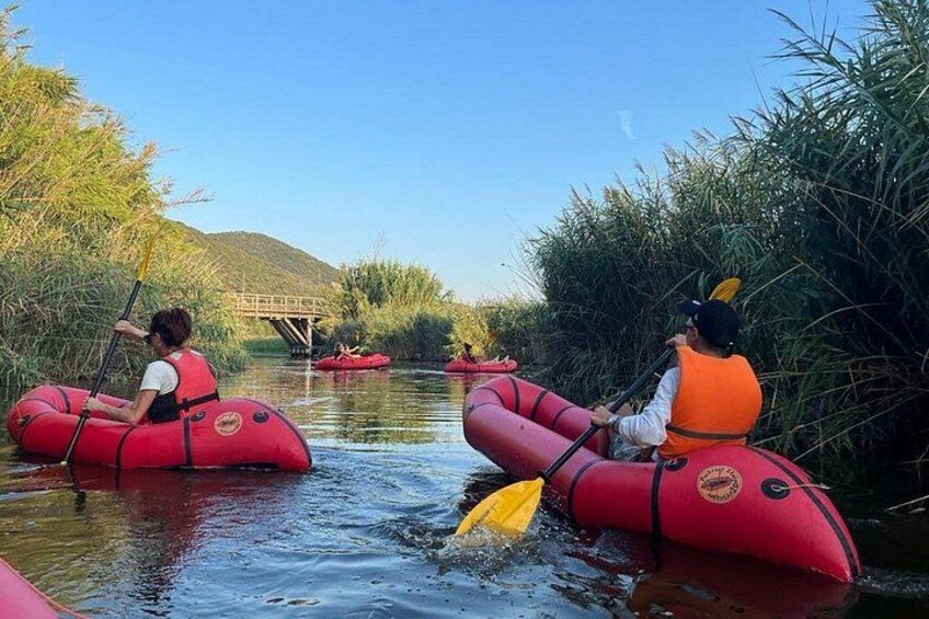 Two people in red inflatable rafts paddling through a river surrounded by greenery. 5