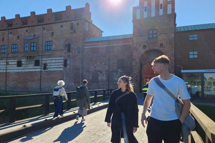 A wooden bridge with people walking on it, a brick building with a tower, and a clear sky. 4