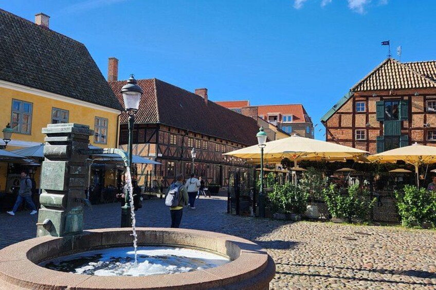 A cobblestone square with a fountain, traditional half-timbered buildings, and outdoor seating areas. 4