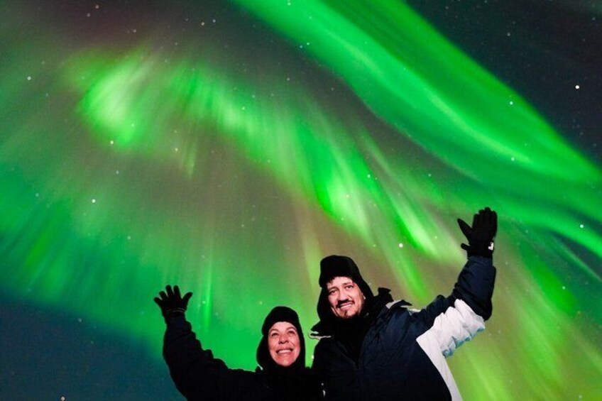 Two people with arms raised, enjoying the Northern Lights. 4