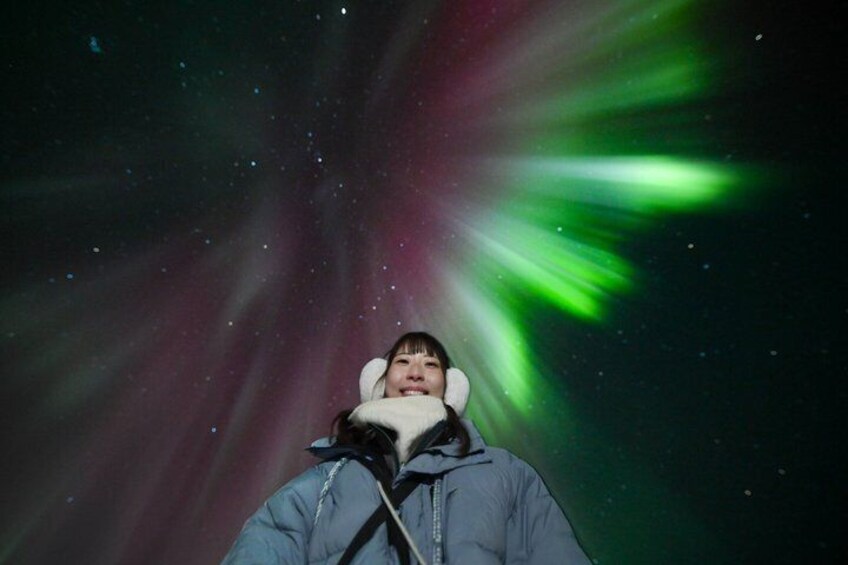 A person wearing a jacket and a hat, standing under a night sky with visible aurora borealis. 3