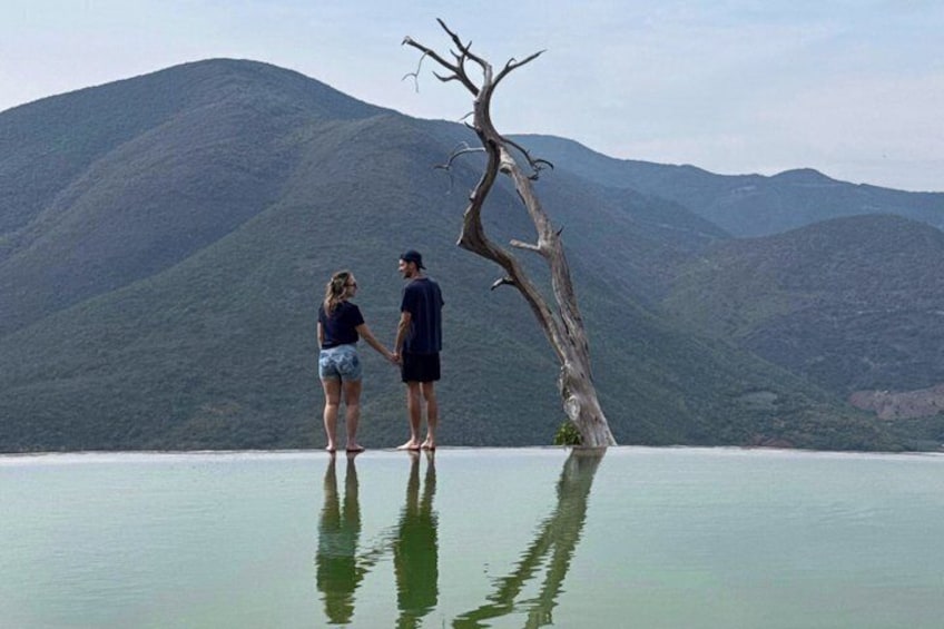 Two people standing by a body of water with a mountain in the background. 1