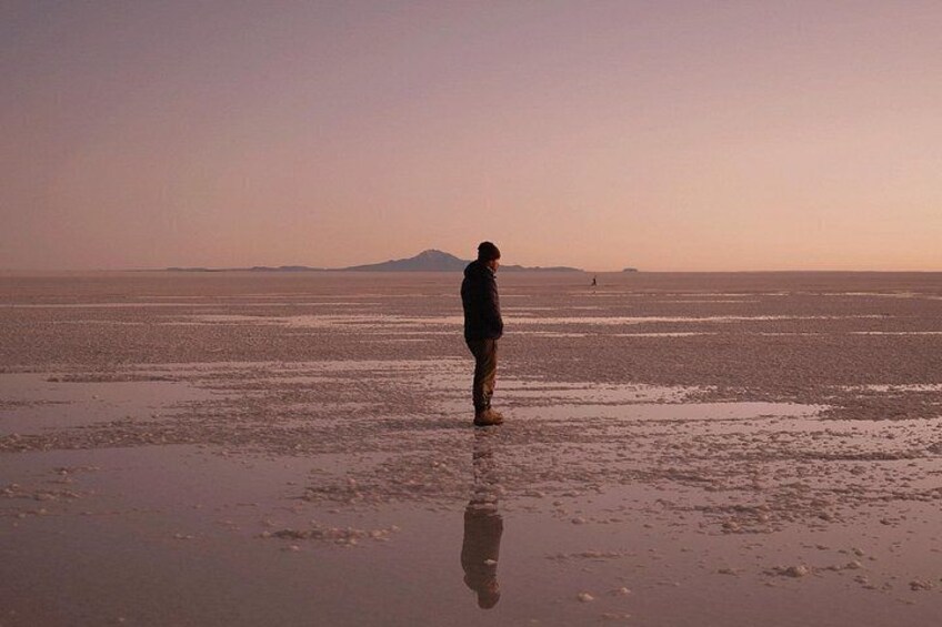 A person standing on a beach with a distant mountain and a calm sea. 1