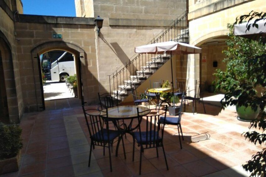 An outdoor café with tables and chairs, a staircase, and a large potted plant. 3