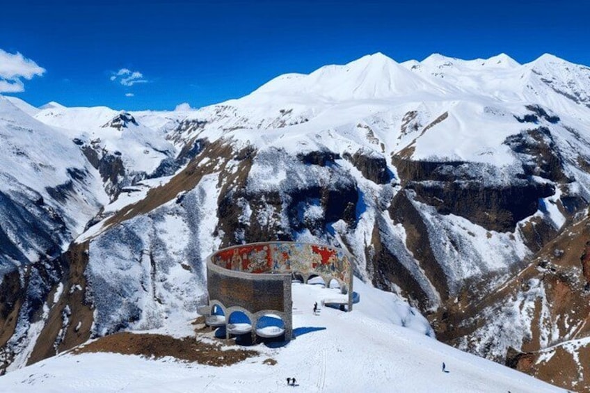 A snow-covered mountain landscape with a large rock structure and a small building. 3