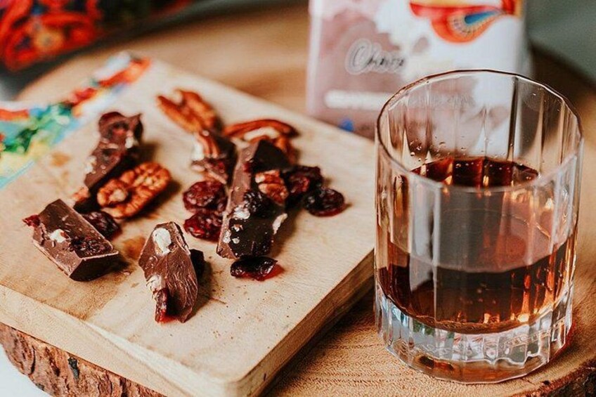 A glass of dark liquid, possibly a beverage, on a wooden surface with chocolate pieces and dried fruits. 2