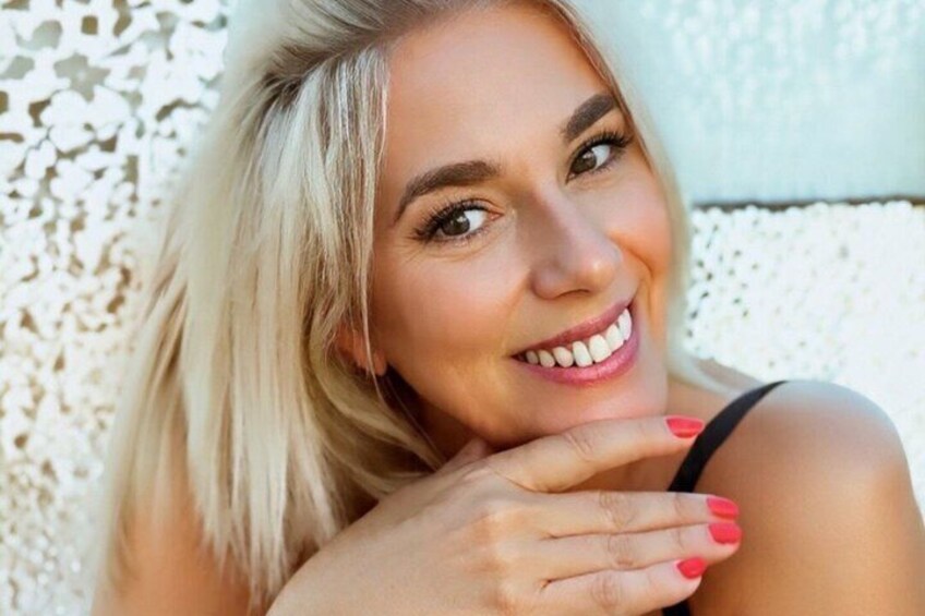 Une personne aux cheveux blonds, vêtue d’un haut noir, a la tête appuyée sur sa main, adossée à un mur blanc à la texture particulière. 5