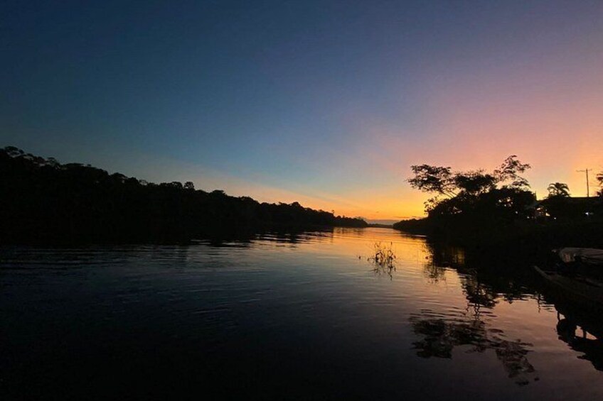 A calm river at sunset with a silhouette of trees and a dock on the right. 3