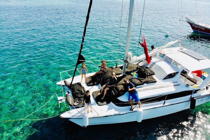 Un velero con gente en la cubierta, agua turquesa cristalina y una pequeña isla al fondo. 1