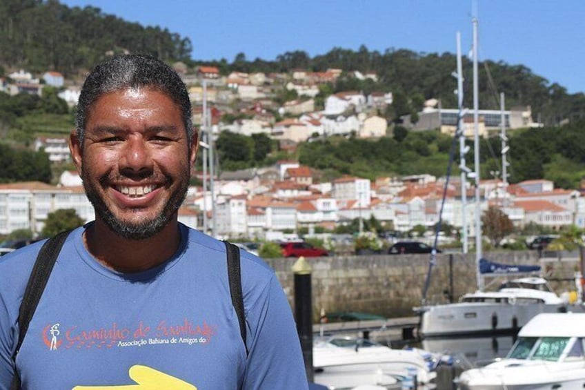 A person standing in front of a marina with boats, a clear sky, and a hillside with buildings in the background. 5