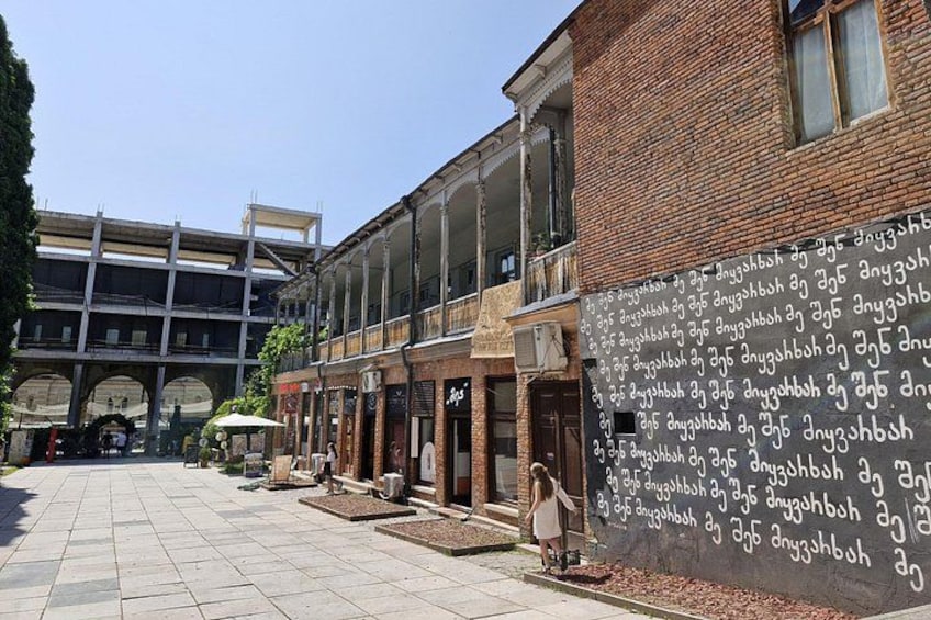 Ein Innenhof mit einem Backsteinhaus, einem Wandgemälde mit Text und einer Person, die dort entlanggeht. 3