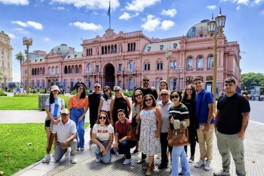 A group of people posing in front of a pink building with a dome and columns. 1