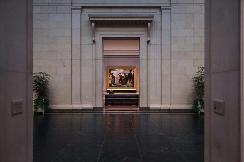 A lobby with a framed painting, a bench, and potted plants. 2