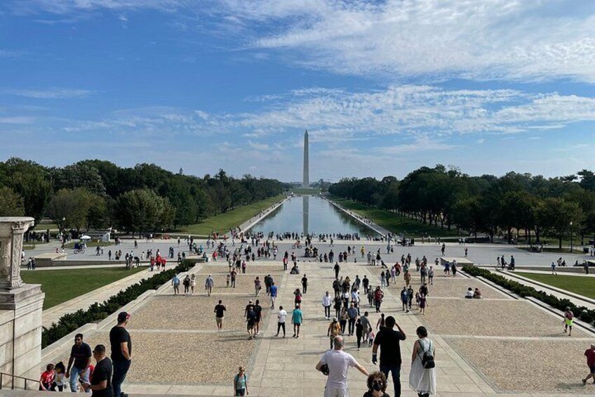 A large open plaza with a central monument, surrounded by trees and a body of water. 4