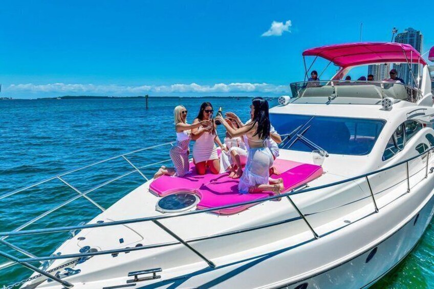 A white yacht with pink mats on the deck, people sitting and sunbathing, and a clear blue sky. 2