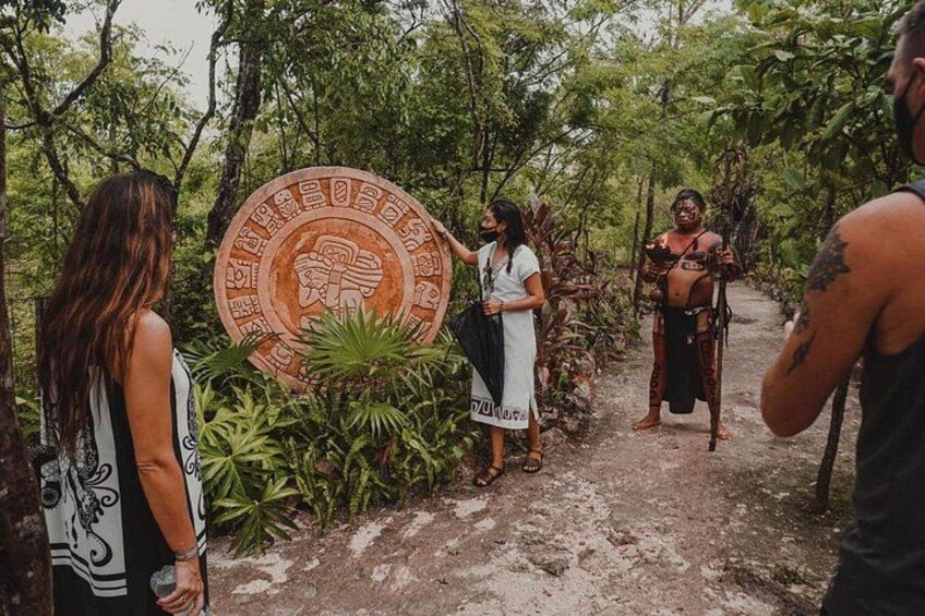 A group of people standing in a forested area with a large circular stone with carvings. 2