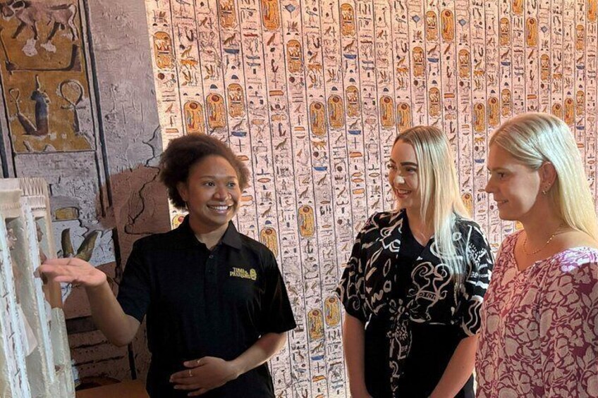 Three people standing in front of an ancient Egyptian wall with hieroglyphs. 1