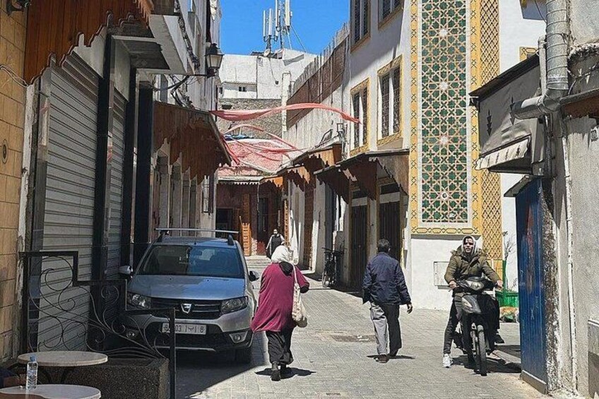 Una calle estrecha con coches aparcados, peatones y arquitectura tradicional. 2