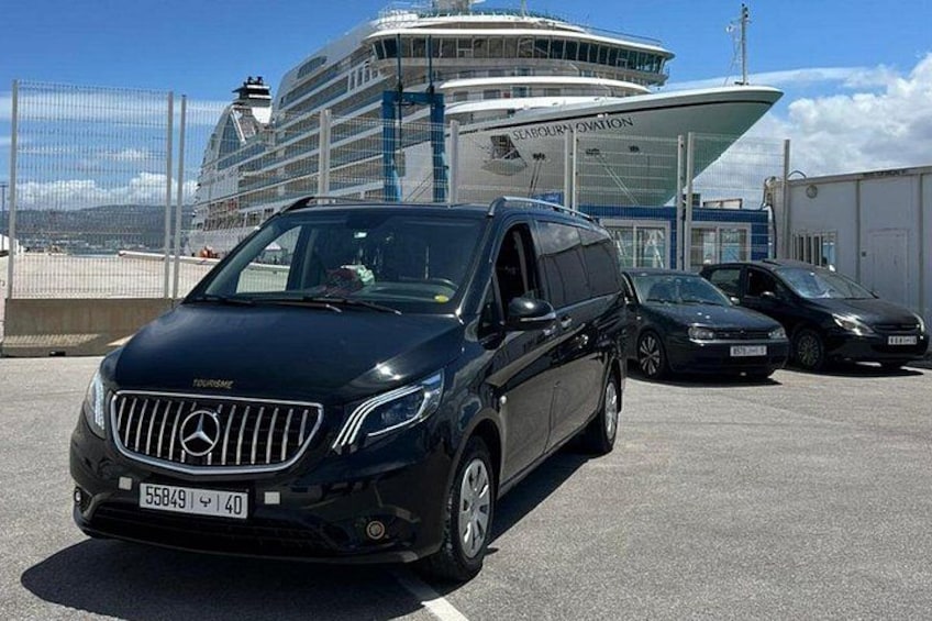 Un SUV Mercedes-Benz noir est garé sur un parking, avec un navire de croisière et un bâtiment portant l'inscription « Scafellburn Aviation » en arrière-plan. 1