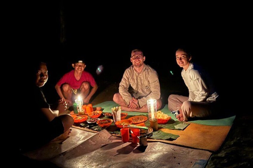 Four people sitting around a table with food and candles at night. 3